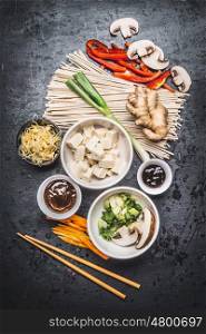 Various Asian vegetarian cooking ingredients and chopsticks with tofu, noodles, ginger, cut vegetables, Sprout,green onion ,hoisin and austern sauce on dark rustic background, top view