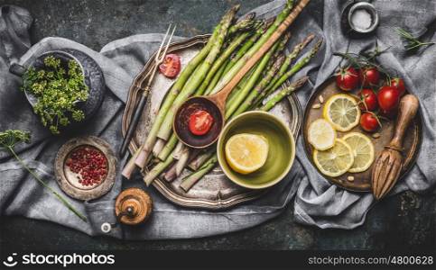 Various asparagus ingredients on rustic kitchen table background with bowls and tools, top view. Dark style