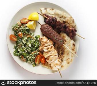 Various barbecued kebabs - kofta, chicken tawook and sumac chicken - with tabouleh and pitta bread; an Arab or Lebanese-style feast, seen from above
