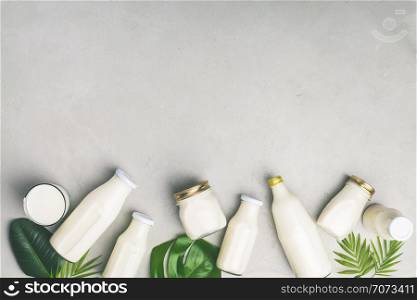 Various bottles of milk and tropical leaves on grey concrete background, flat lay. Vegan, vegetarian or clean eating concept
