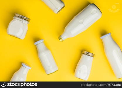 Various bottles of milk on yellow background, flat lay