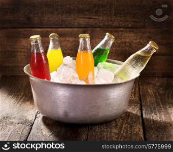 various bottles of soda in the bucket with ice on wooden table