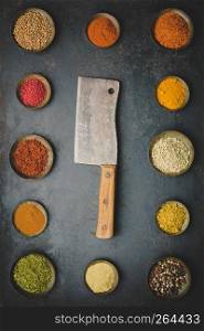 Various bowls of spices and meat knife over dark background, cooking concept - flat lay