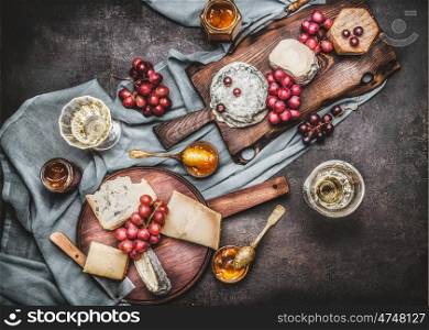 Various cheese served on rustic cutting boards with grape and wine, dark vintage background, top view