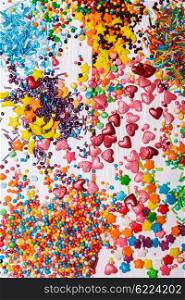 Various color sprinkles scattered on white wooden table. The color sprinkles