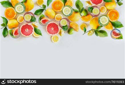 Various colorful citrus fruits: lemon, lime, orange and grapefruit with green leaves and glasses of refreshing lemonade drinks on white background, top view. Healthy lifestyle. Border or frame.