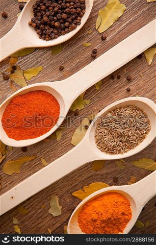 Various colorful dried spices in white spoons on the wooden background - pepper, curry, chilli, caraway