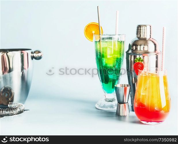 Various colorful long drinks and cocktails bar tools at light blue background, copy space. Summer alcoholic beverages