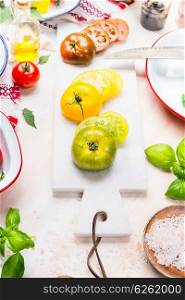 Various colorful tomatoes cooking. Various colorful tomatoes for salad preparation on light background with marble cutting board.