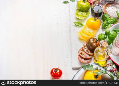 Various Colorful tomatoes with bottle of oil and salad vinaigrette, basil and spices on white wooden background, top view, border