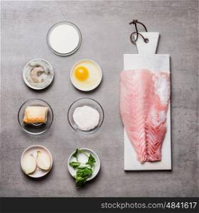 Various cooking ingredients for Fish patties in bowls: fish fillets , egg, shrimps , onion ,bread, flour on on gray stone background , top view