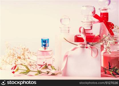 Various cosmetic products bottles and jars with flowers and empty paper card with ribbon for Invitation, coupon, discount and sale, front view. Beauty, skin and hair care concept