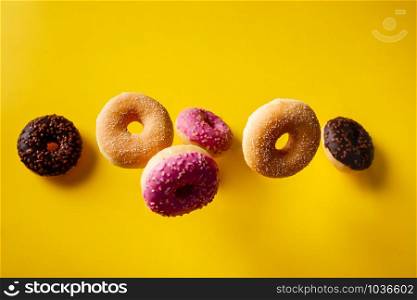 Various decorated doughnuts in motion falling on yelloy background. Sweet and colourful doughnuts falling or flying in motion.. Various decorated doughnuts in motion falling on yelloy background