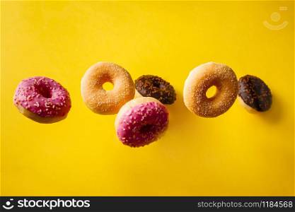 Various decorated doughnuts in motion falling on yelloy background. Sweet and colourful doughnuts falling or flying in motion.