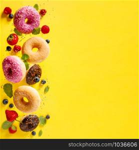 Various decorated doughnuts with sprinkles and berries in motion falling on yelloy background. Sweet and colourful doughnuts falling or flying in motion.. Various decorated doughnuts with sprinkles and berries in motion falling on yelloy background