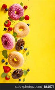Various decorated doughnuts with sprinkles and berries in motion falling on yelloy background. Sweet and colourful doughnuts falling or flying in motion.