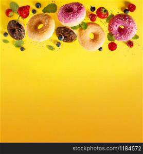 Various decorated doughnuts with sprinkles and berries in motion falling on yelloy background. Sweet and colourful doughnuts falling or flying in motion.