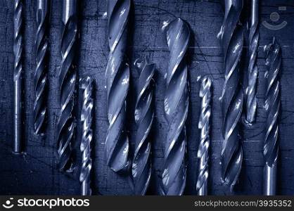 Various drills on a metallic, old, rough background. Macro. Toned blue.
