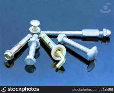 Various equipment: screw bolts and bolts with washers on a glossy dark blue surface of a metal background design.. Screwbolts screw nuts, hanger and bolt washers on blue background construction concept.