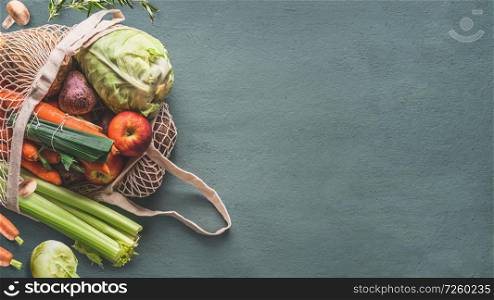 Various farm organic vegetables from local market in net string reusable bag on rustic background, top view with copy space for your design, banner. Clean and healthy food concept