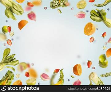 Various flying or falling summer fruits,berries and vegetables on light blue background, frame. Healthy detox food layout concept