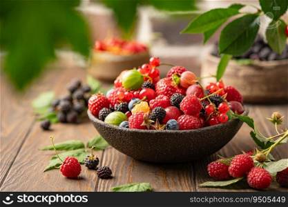 Various fresh berries in a bowl. Mix of different fresh berries on wooden background. Strawberries, raspberries, gooseberries and cherries are presented.. Various fresh berries