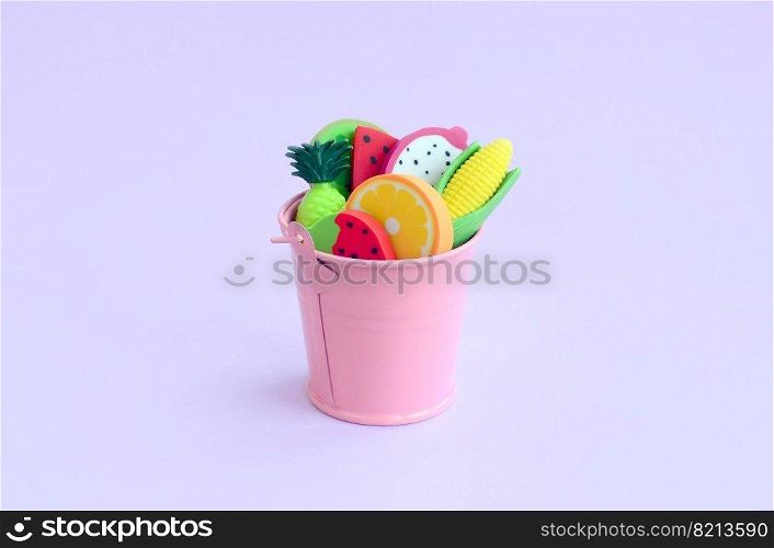 Various fresh fruits in a small pink pail on violet background. Seasonal fruit harvest. Work for farmers. Various fresh fruits in small pink pail on violet background