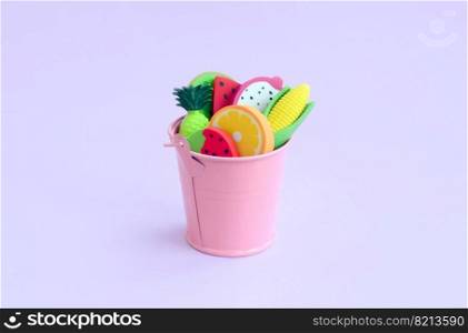 Various fresh fruits in a small pink pail on violet background. Seasonal fruit harvest. Work for farmers. Various fresh fruits in small pink pail on violet background