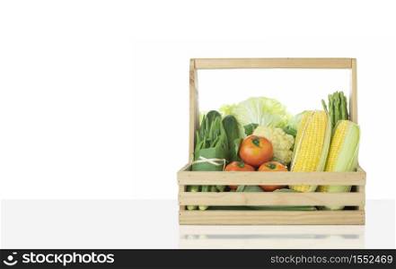 Various fresh organic vegetables in wooden basket on grey tabletop with white wall background