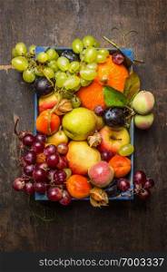 various fresh sharvest fruits in a blue box on a dark wooden texture, top view