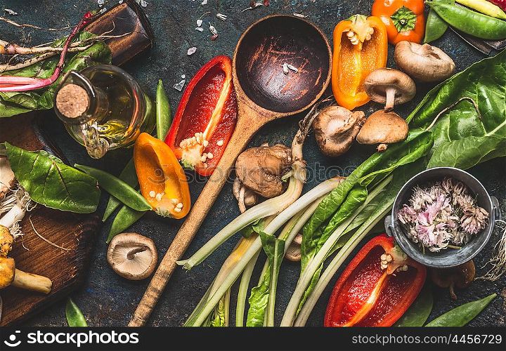 Various fresh vegetables with wooden cooking spoon for healthy eating and nutrition on dark rustic background, top view