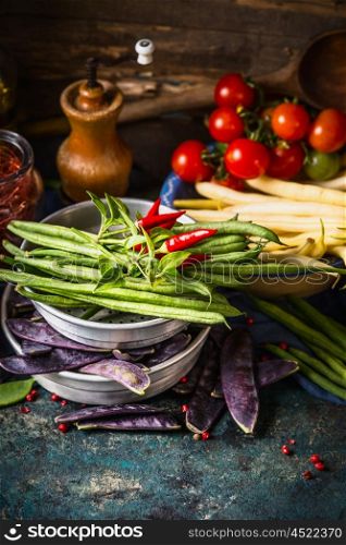 Various green and white beans pods in bowls with cooking ingredients on dark rustic kitchen table with wooden background.