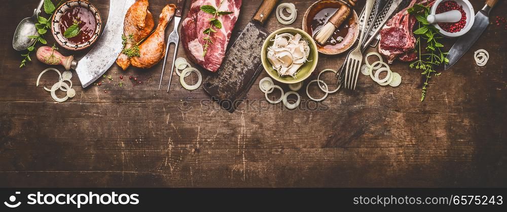 Various grill an bbq meats on rustic wooden background with aged kitchen and butcher tools, herbs, spices, seasoning and sauce, top view, border
