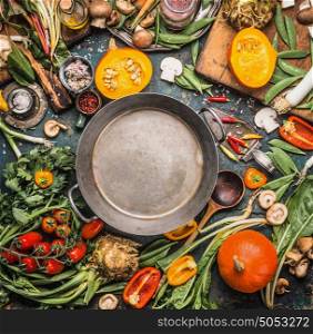 Various Healthy and organic harvest vegetables and ingredients: pumpkin, greens, tomatoes,kale,leek,chard,celery around empty cooking pot for tasty Thanksgiving seasonal cooking, top view, frame
