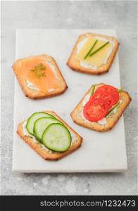 Various healthy crackers with salmon and cheese, tomato and cucumber on marble board on light table background.