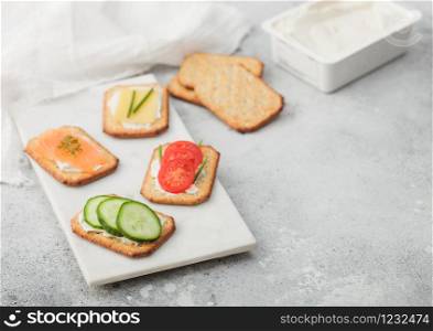 Various healthy crackers with salmon and cheese, tomato and cucumber on marble board on light table background. Top view