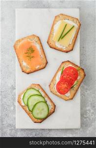 Various healthy crackers with salmon and cheese, tomato and cucumber on marble board on light table background. Top view