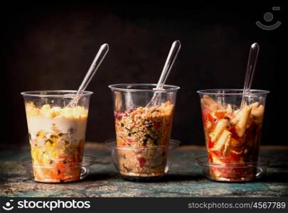 Various Healthy lunch salad in plastic cups on dark background, side view