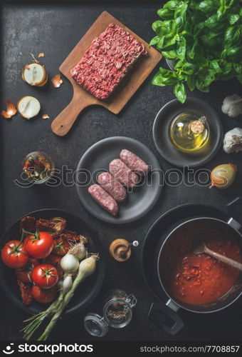Various ingredients for  Sauce bolognese : Salsiccia sausages, minced meat, tomatoes sauce, herbs and spices on dark kitchen background. Top view. Cooking preparation