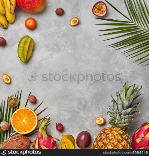 Various juicy exotic fruits, coconut, lychee, carom, pineapple and palm leaves on a gray concrete background with space for text. Food layout. Flat lay. Bright composition of different exotic fruits and palm green leaves on a gray concrete background with copy space. Food background. Flat lay