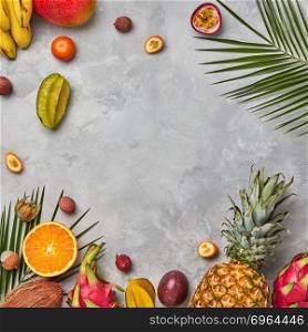 Various juicy exotic fruits, coconut, lychee, carom, pineapple and palm leaves on a gray concrete background with space for text. Food layout. Flat lay. Bright composition of different exotic fruits and palm green leaves on a gray concrete background with copy space. Food background. Flat lay