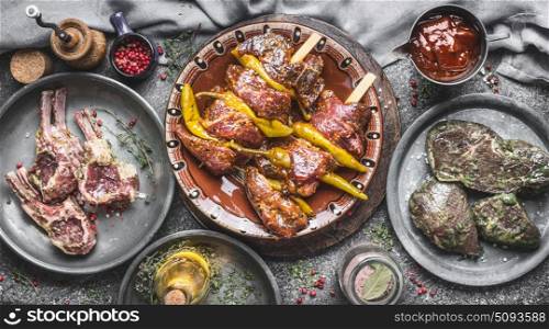 Various meat for grill: meat skewers , lamb racks ribs and marinated steaks on rustic kitchen table background, top view, cooking preparation