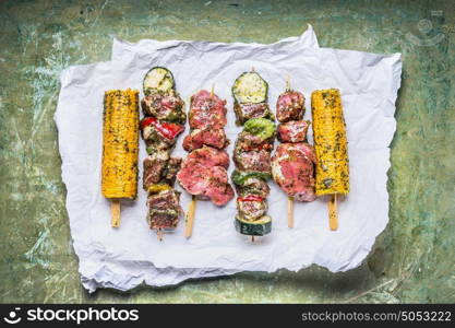 Various Meat Skewers for grill with vegetables , corn ears and condiment on green rustic background , top view