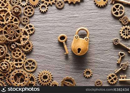 Various metal cogwheels and gear wheels with lock and key over slate background