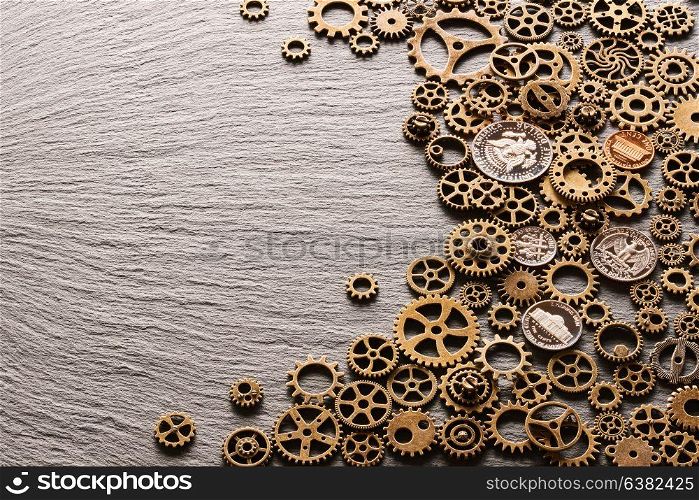 Various metal cogwheels and gear wheels with USA coins over slate background