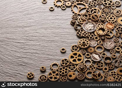 Various metal cogwheels and gear wheels with USA coins over slate background