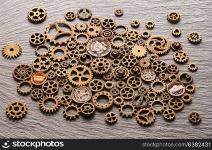 Various metal cogwheels and gear wheels with USA coins over slate background