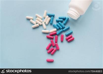 Various multicolored pills - blue, pink, white flying from an open plastic bottle, isolated on a light blue background. Various multicolored pills - blue, pink, white flying from an open plastic bottle, isolated on a light blue background.