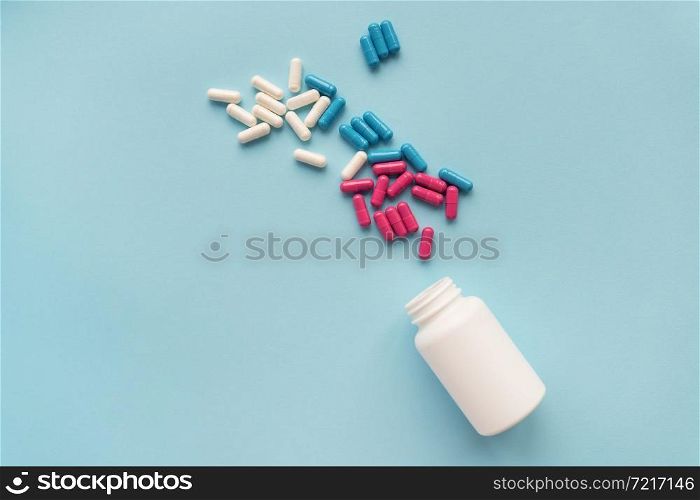 Various multicolored pills flying from an open plastic bottle isolated on a blue background. Various multicolored pills flying from an open plastic bottle isolated on a blue background.