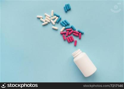 Various multicolored pills flying from an open plastic bottle isolated on a blue background. Various multicolored pills flying from an open plastic bottle isolated on a blue background.